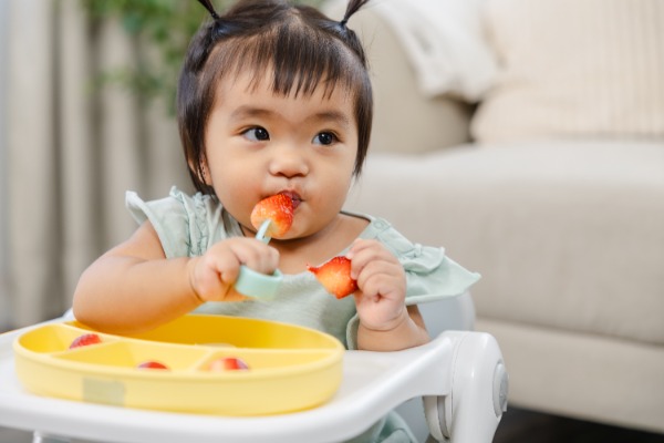 adorable asian child sitting in a high chair eating strawberries