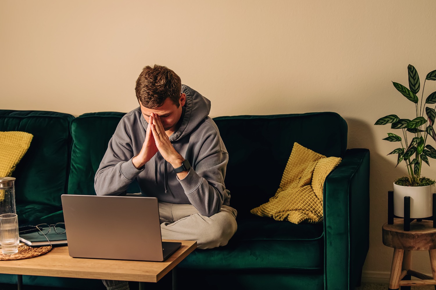 Sad, frustrated man sitting on the green couch in his living room in front of his laptop