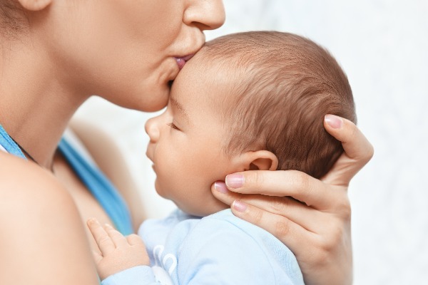 white mother holding her baby and kissing her forehead
